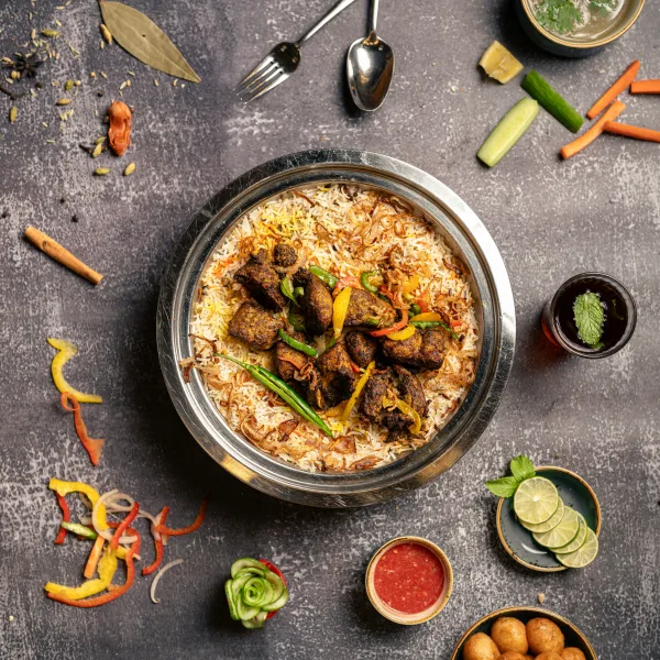 Pot of Pakistani beef pulao with golden basmati rice, beef pieces, browned onions and fresh herbs