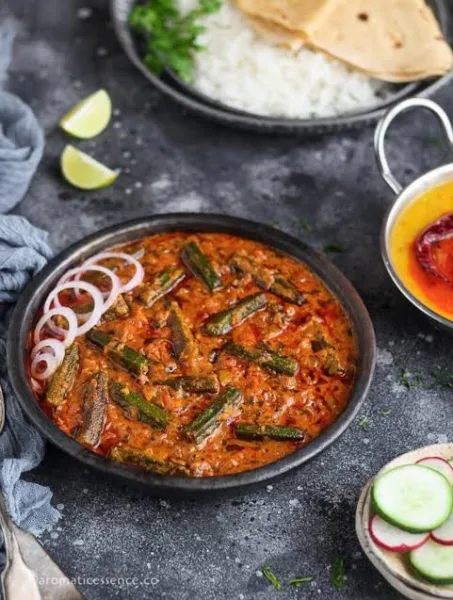 A pan of bhindi masala with okra in a thick onion-tomato masala, garnished with coriander and ginger, served with roti.