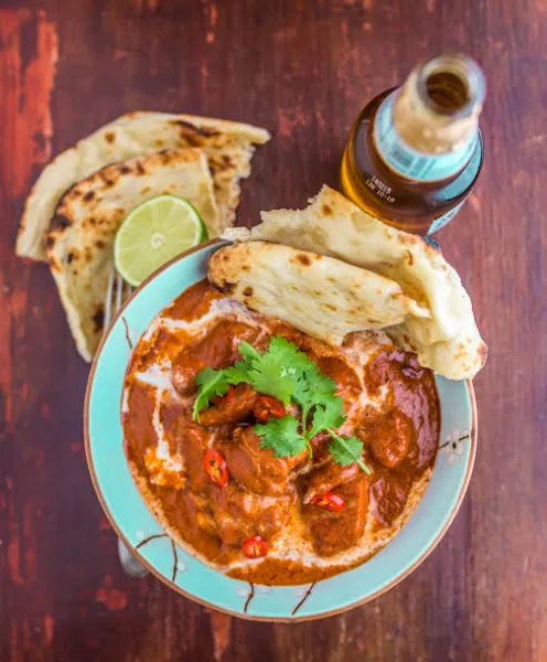 Bowl of creamy butter chicken with cream swirl and fresh coriander, served with naan and rice