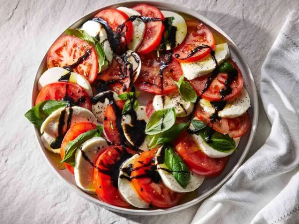 Caprese salad of sliced tomatoes, mozzarella and basil on a white platter with balsamic glaze