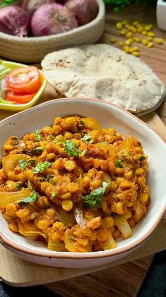 Bowl of golden chana daal topped with garlic tarka, chillies and fresh coriander, served with rice and roti