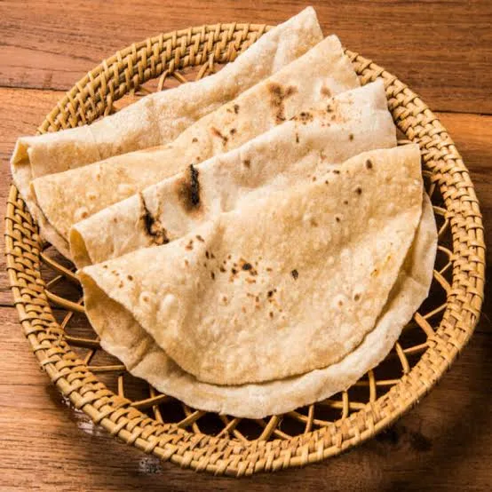 Stack of freshly cooked soft chapatis with golden spots on a wooden board beside a bowl of ghee