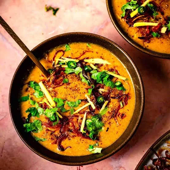 Bowl of Pakistani chicken haleem topped with fried onions, ginger, green chillies, herbs and lemon wedges