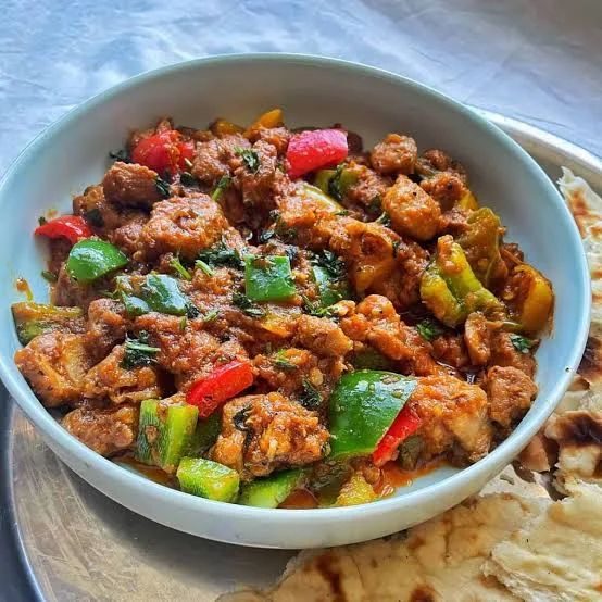 A pan of chicken jalfrezi with red and green peppers, onion wedges and fresh ginger in a thick tomato masala