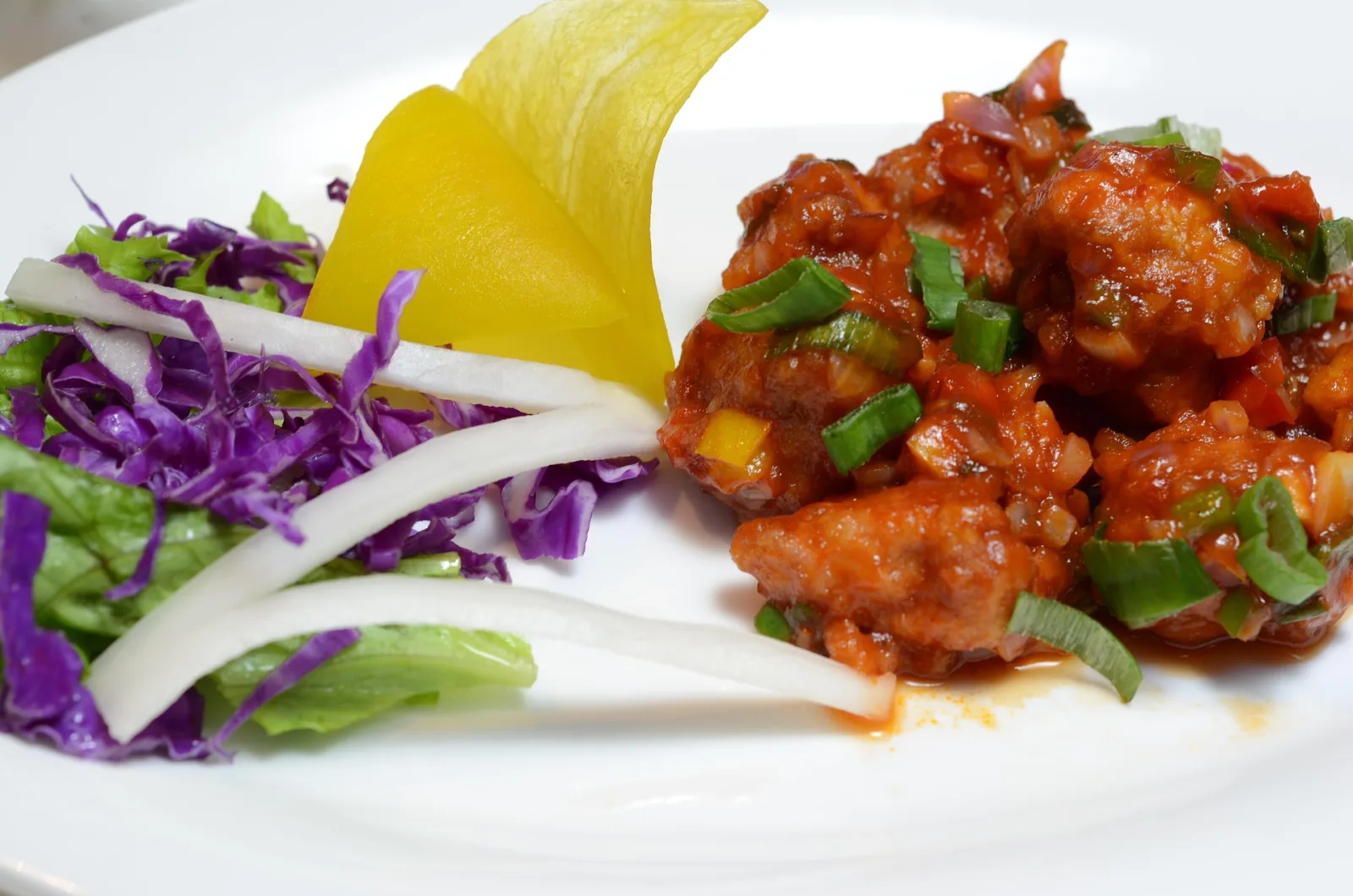 A white bowl of glossy chicken Manchurian with capsicum, onion and spring onion, served next to fried rice