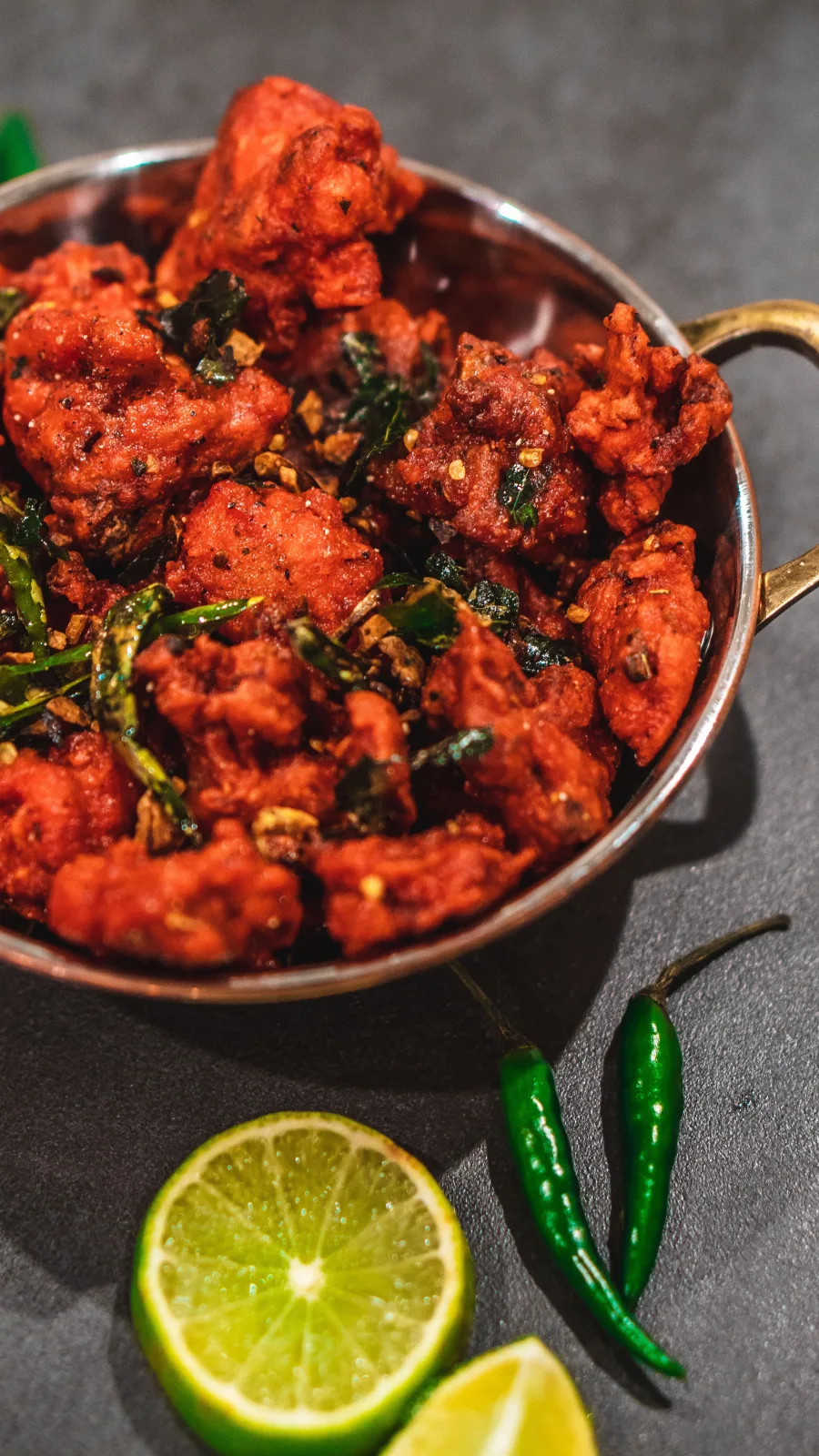 A plate of golden fried chicken pakoras with mint chutney, lemon wedges and onion rings