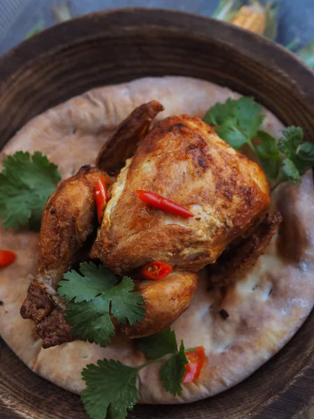 Whole roasted chicken sajji with spiced rice stuffing, roasted potatoes and lemon wedges on a wooden board