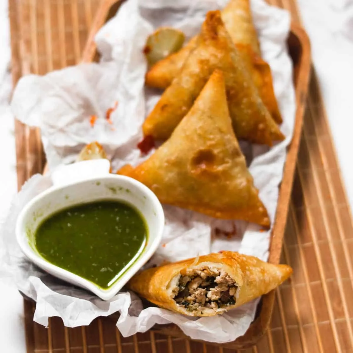 Golden fried chicken samosas on a plate with one split open showing spiced chicken mince, served with chutneys