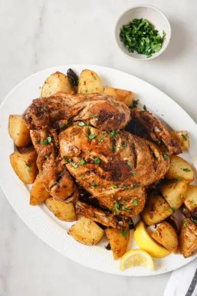 Golden roasted chicken pieces on a tray with onion gravy, green chillies and lemon wedges