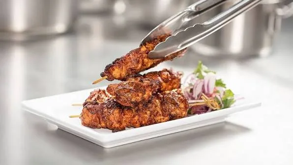 Skewers of charred, red-orange chicken tikka boti served with onions, lemon wedges, chutney and naan