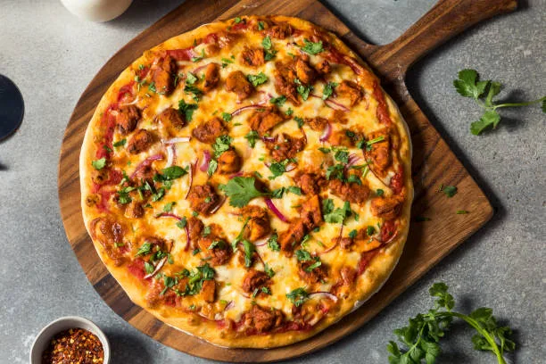 Chicken tikka pizza topped with mozzarella, peppers, onion and coriander on a wooden board