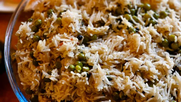 Golden chicken yakhni pulao topped with fried onions and mint, served in a wide dish with raita and salad