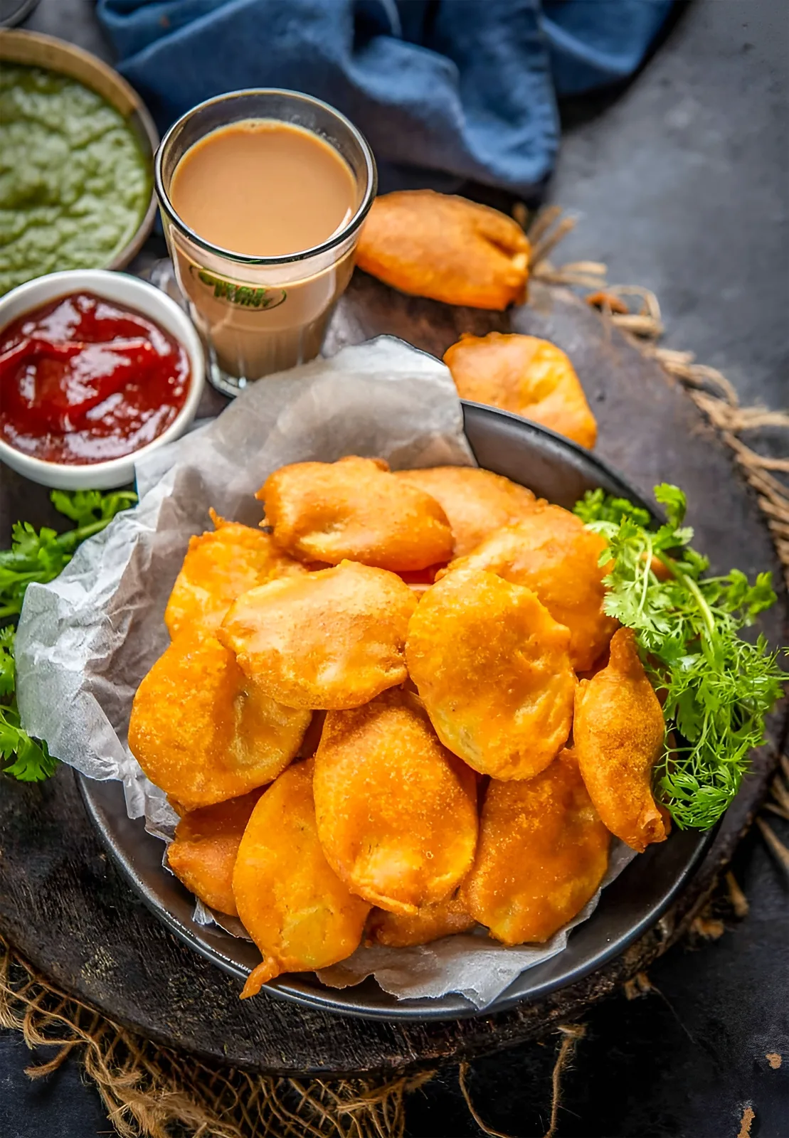 A plate of golden crispy fish pakoras with mint chutney, tamarind chutney and lemon wedges