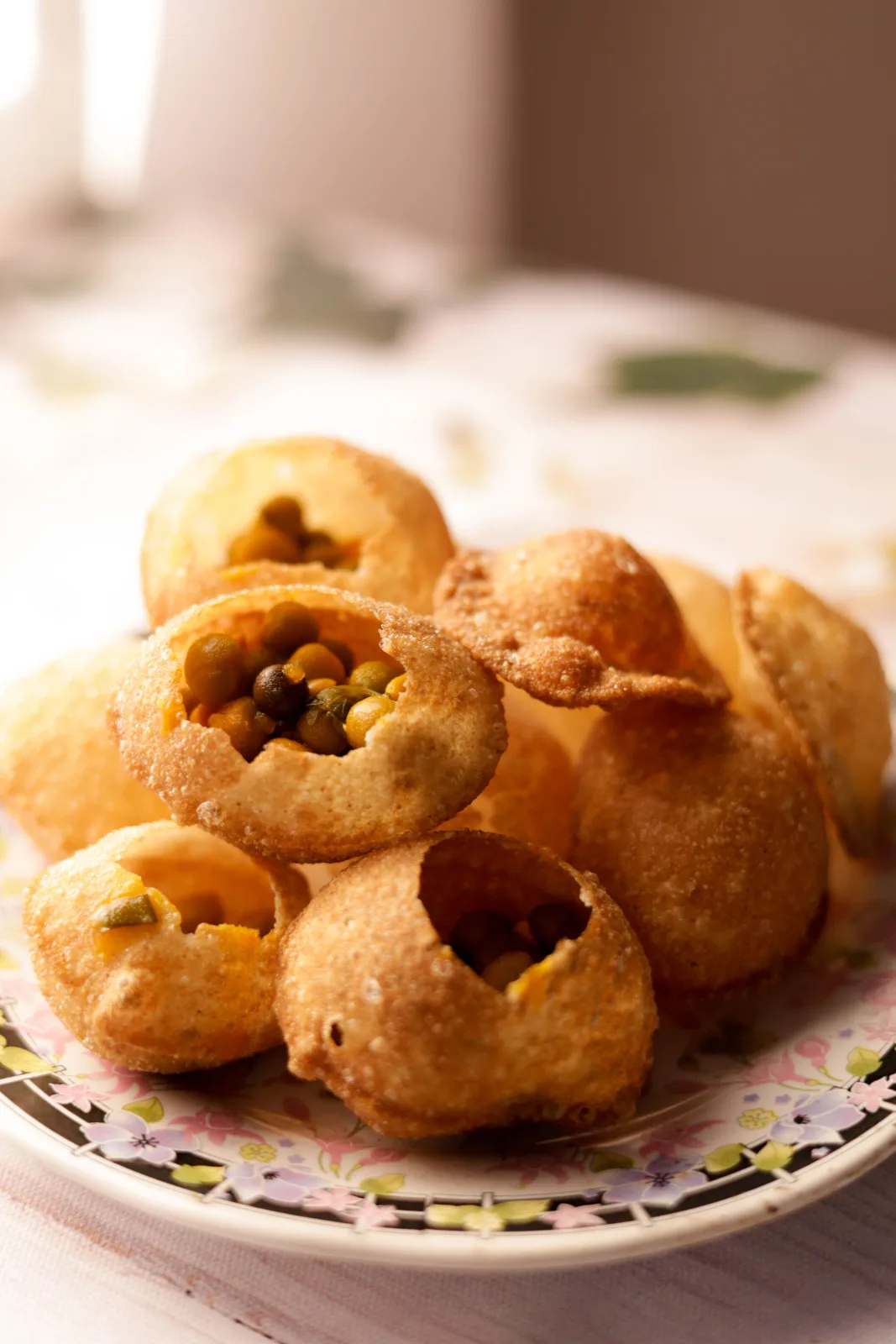 Golden gol gappay shells on a platter with a jug of green mint pani and bowls of chickpea filling