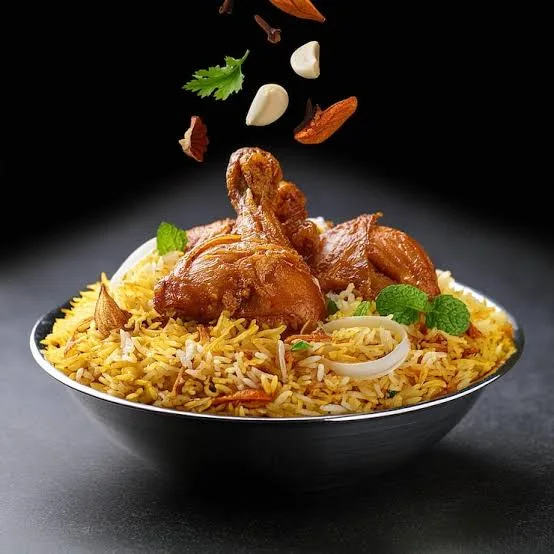 Open pot of Hyderabadi chicken biryani with saffron rice, chicken pieces, fried onions and fresh herbs