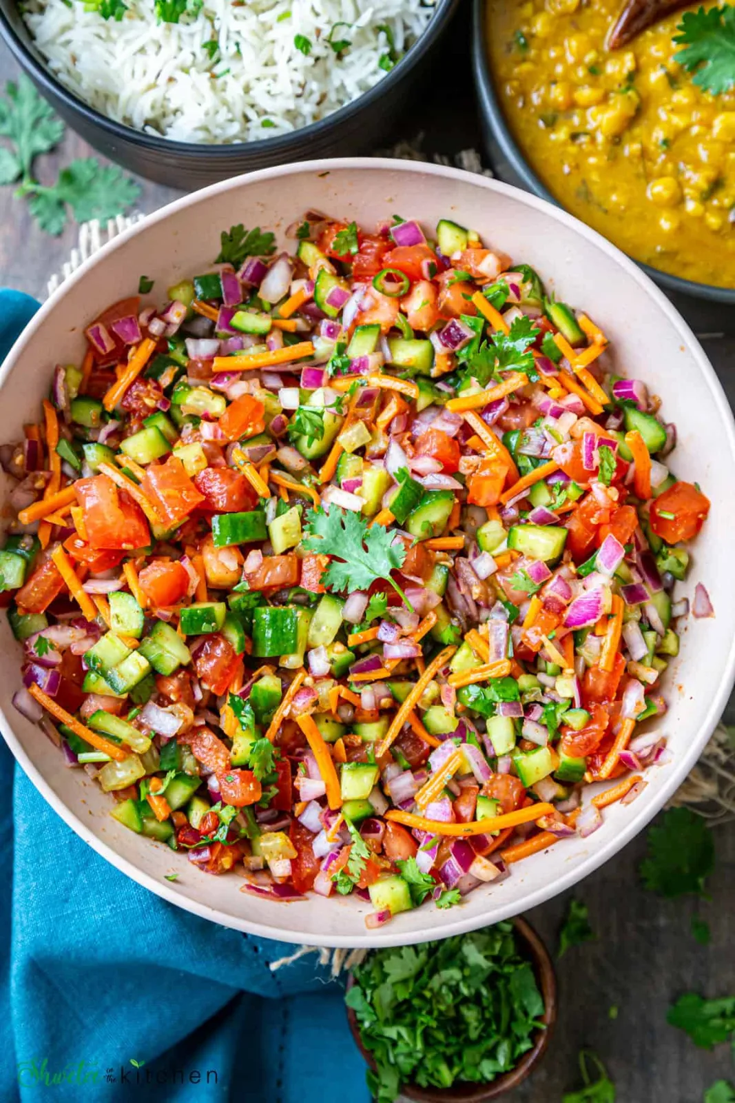 Bowl of diced cucumber, tomato and red onion salad with coriander, mint and pomegranate seeds beside lemon halves