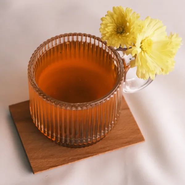 Glass cups of golden Kashmiri kahwa tea topped with sliced almonds, beside a teapot, cinnamon sticks and cardamom pods