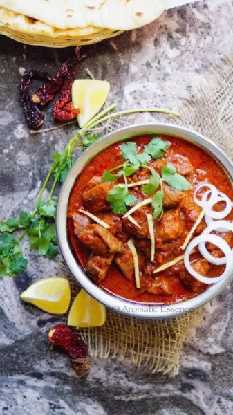 Brass pot of deep red Laal Maas mutton curry garnished with coriander, served with bajra roti and onions