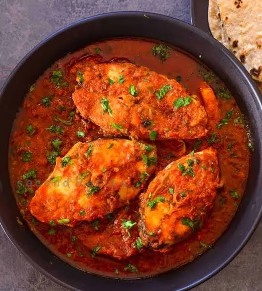 Pan of Pakistani masala fish curry with fish steaks in red tomato gravy, green chillies and fresh coriander, served with rice