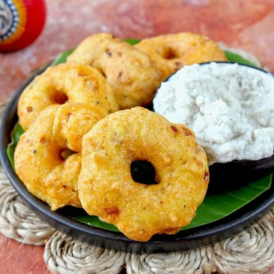Golden medu vada doughnut-shaped fritters on a plate with coconut chutney and sambar, one broken open to show a soft centre