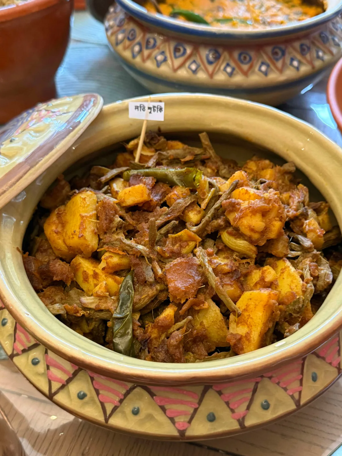 A pot of mixed vegetable curry with potato, carrot, green beans, cauliflower and peas in a red-orange masala, served with roti