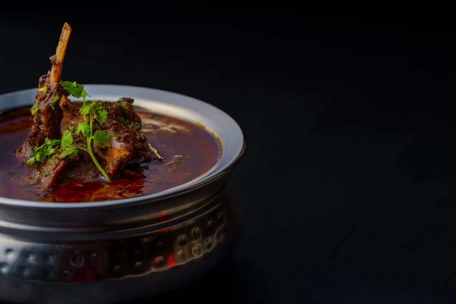 A karahi of mutton in a thick red tomato masala, garnished with ginger, green chillies and fresh coriander, served with naan.