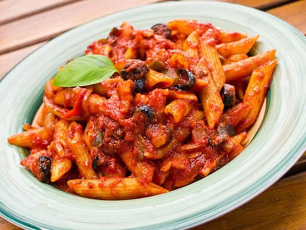 A bowl of penne arrabbiata in a glossy red chilli tomato sauce topped with parsley and cheese