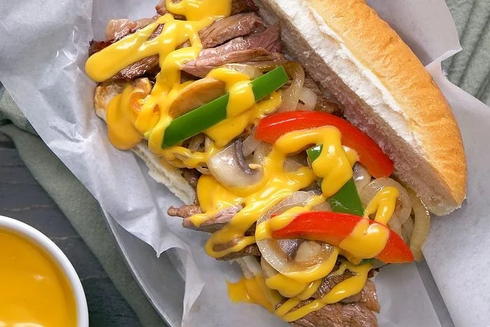 Two Philly cheesesteak sandwiches filled with sliced beef, onions and melted cheese on a wooden board