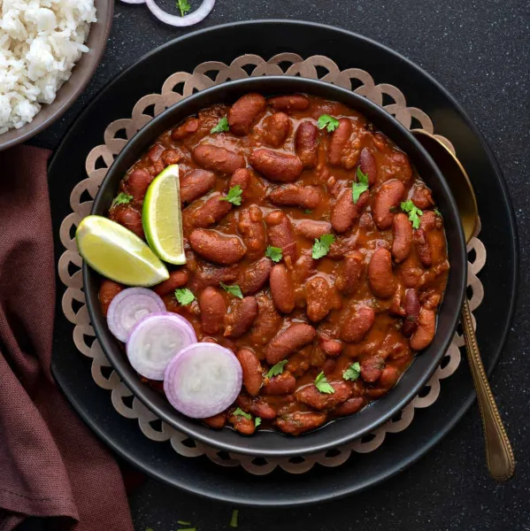 A bowl of rajma masala, red kidney beans in a thick spiced tomato gravy, served with basmati rice, onion and lemon.