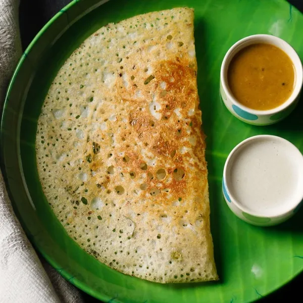 Crisp golden lacy rava dosa folded on a plate with coconut chutney, tomato chutney and sambar