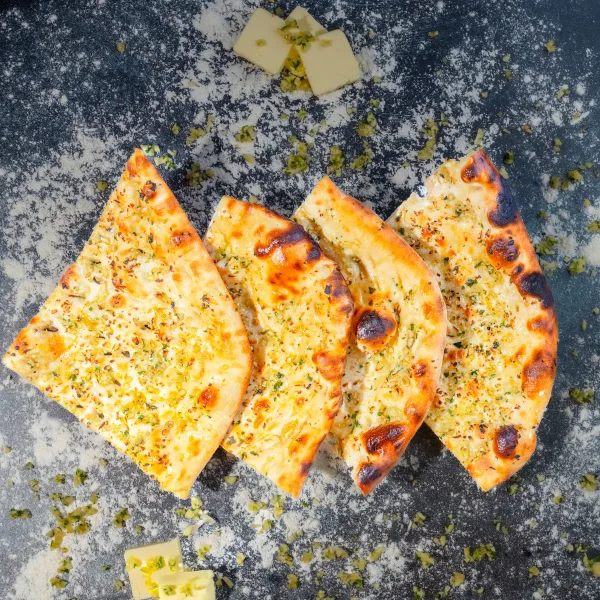 Freshly baked roghni naan topped with sesame and nigella seeds on a wooden board