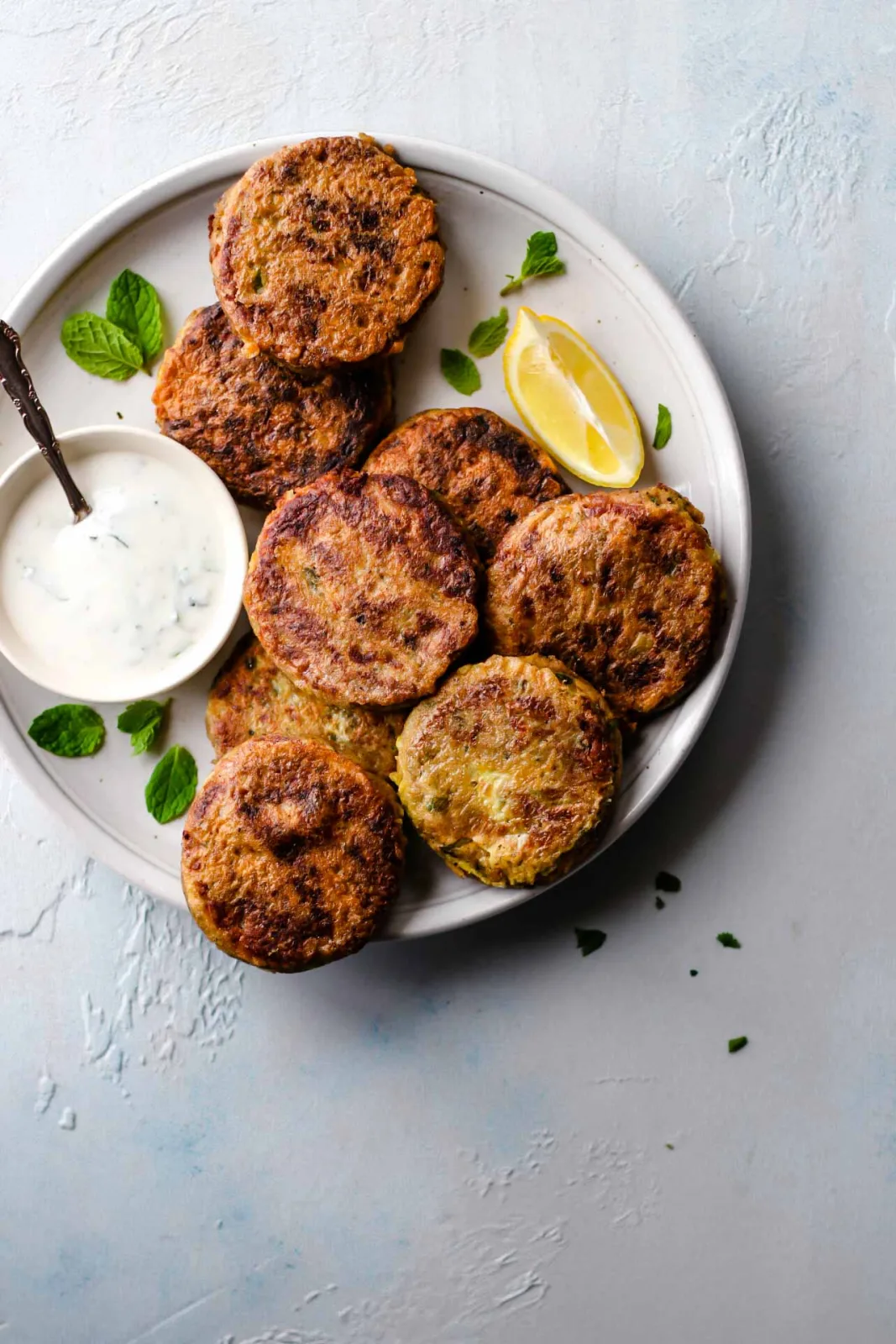 Golden shallow-fried shami kababs on a plate with green chutney, lemon wedges and sliced onions