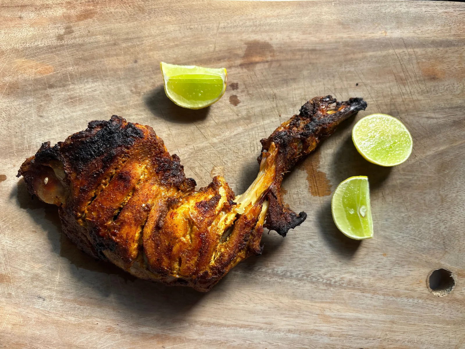 Charred red tandoori chicken legs served with onion rings, lemon wedges and green chutney